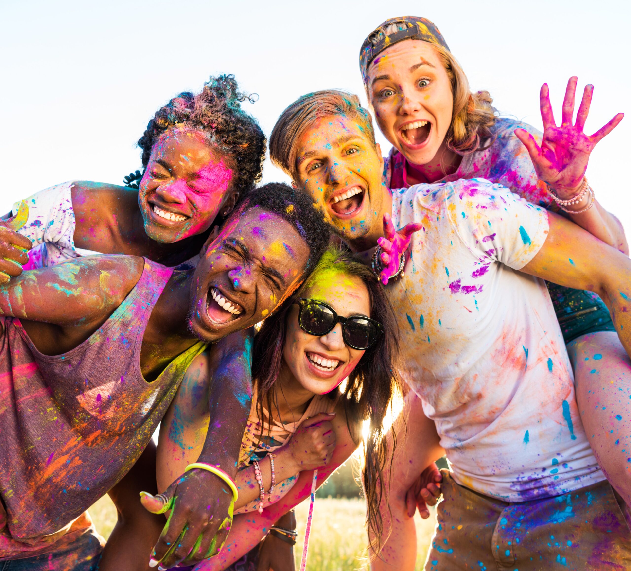 happy young multiethnic friends with colorful paint on clothes having fun together at holi festival